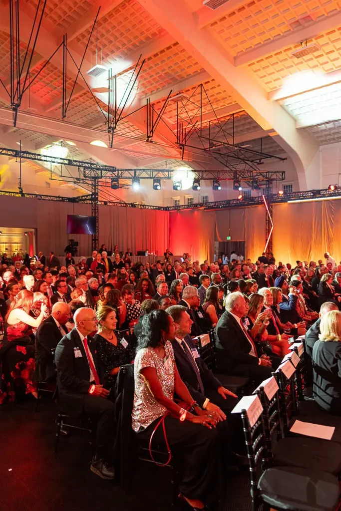 Full ballroom audience at a Washington DC corporate fundraising event with red stage lighting and executive attendees