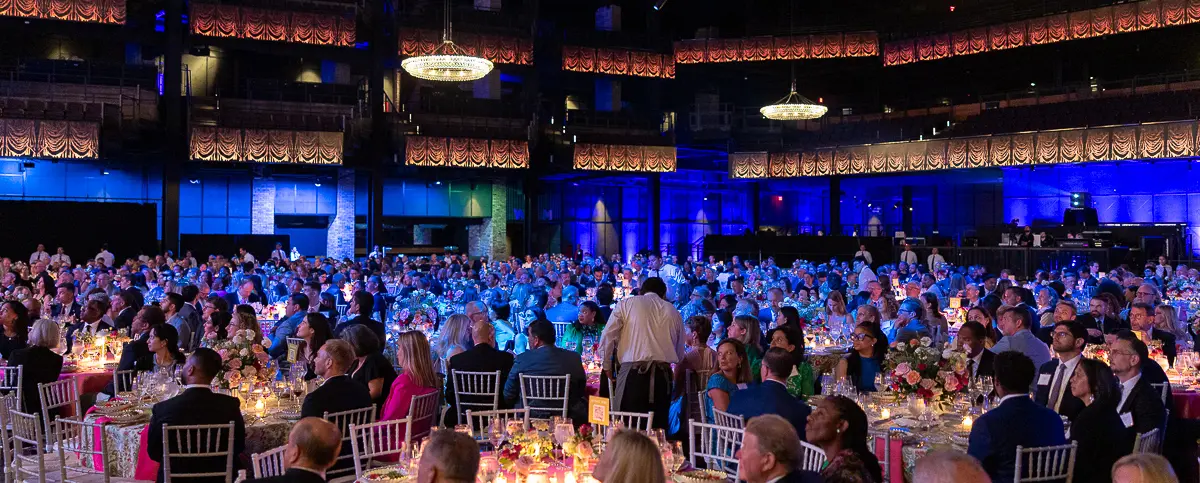 Blue-lit Washington DC gala audience with dinner tables, chandeliers, and full-room event coverage