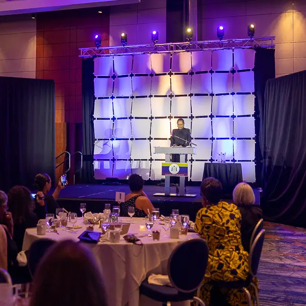 Corporate event keynote speaker presenting on stage at a gala dinner in Washington DC with audience seated at round tables