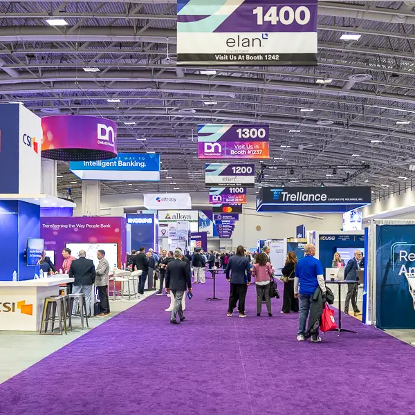Attendees walking through exhibition booths at a large trade show expo inside a convention center