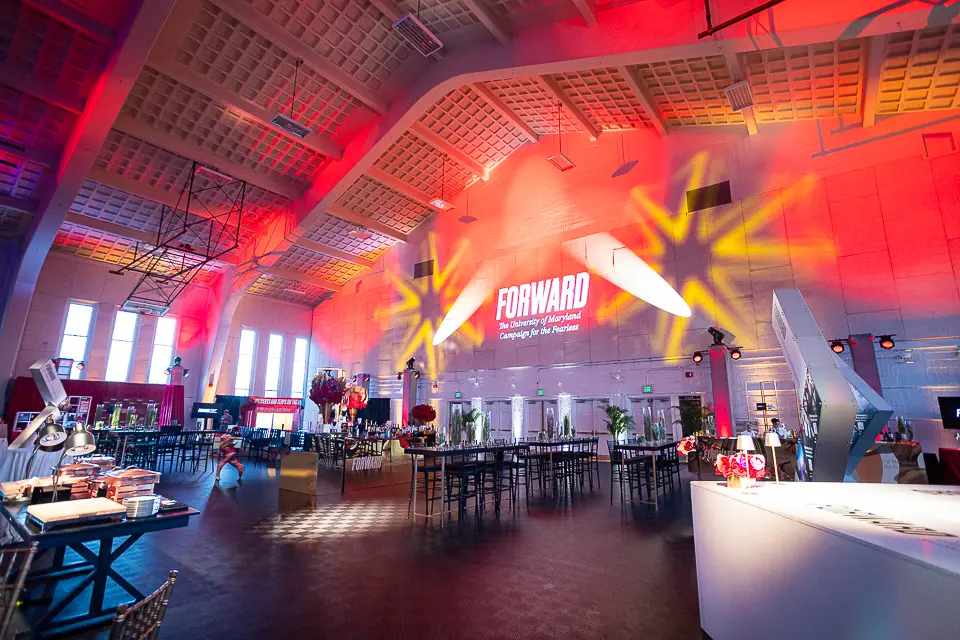 Wide University of Maryland Forward reception room with stage branding, bar stations, and colorful ceiling lighting