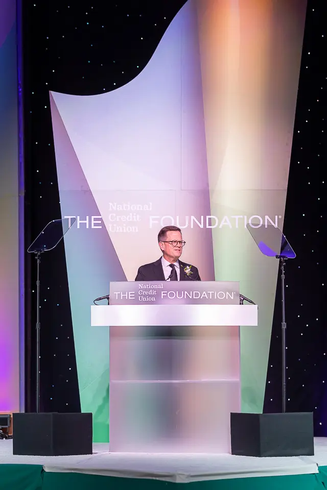 Podium speaker photographed vertically on the lit Herb Wegner Awards 2026 stage.