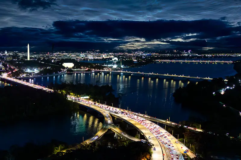 Long exposure night photography of the Washington DC skyline and Potomac River bridges with traffic light trails.