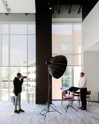Behind-the-scenes corporate headshot session with a professional photographer capturing executive portraits in a modern office space using studio lighting